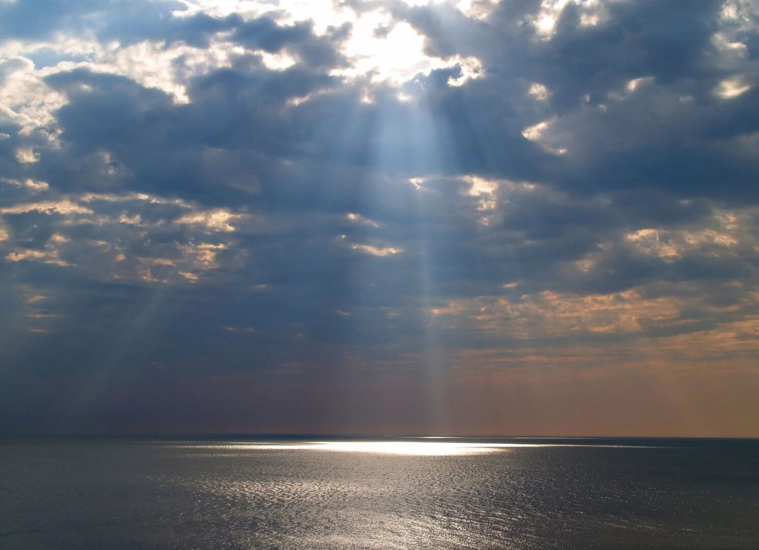 A sun beam shining through the clouds over an ocean.