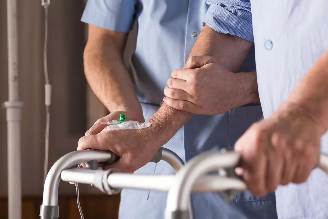 Two men holding hands while standing next to a walker.